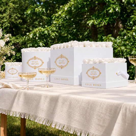 White preserved rose boxes by LULU ROSÉE displayed on a garden table with champagne.