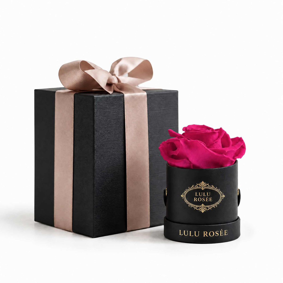 A deep pink eternal rose in a black Mini Round box beside a wrapped gift box.
