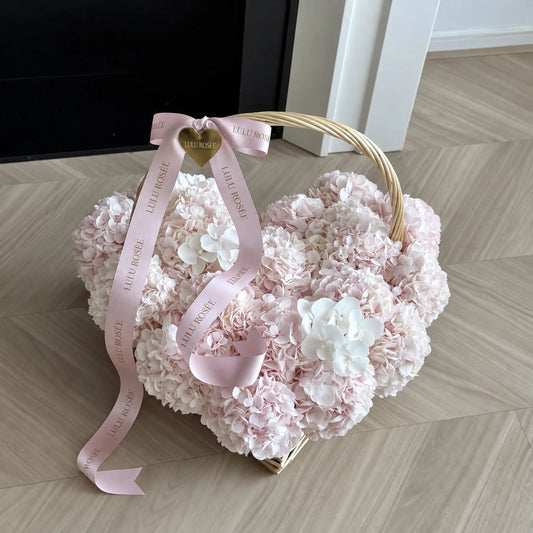Petite heart-shaped preserved hydrangea basket with a pink bow displayed indoors