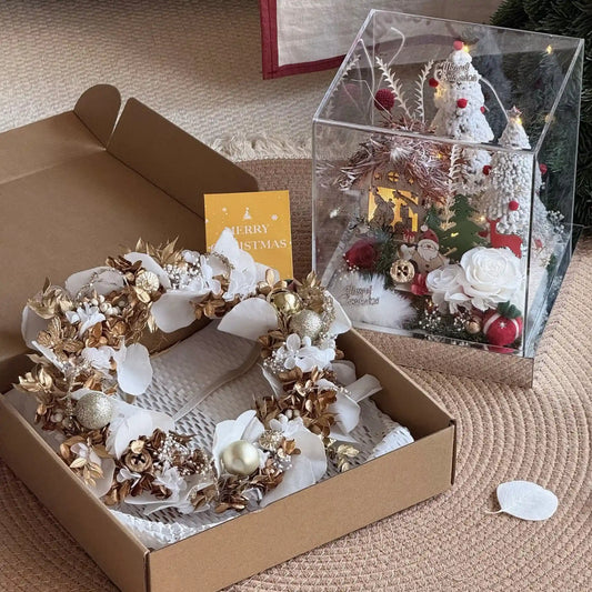 Preserved flower wreath in an open gift box beside a separate Christmas village display.