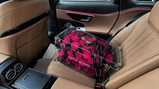 LULU ROSÉE grande transparent acrylic handbag rose box filled with fuchsia preserved roses placed on luxury car seat, premium unique romantic flower gift ideas for women special occasions