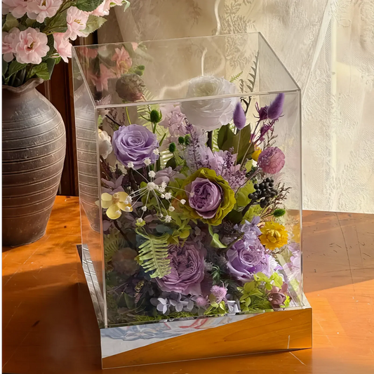 Purple, green and cream preserved flowers displayed in a clear acrylic box in a refined home interior.