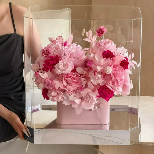 A model holding a clear box filled with blush-pink preserved roses and mixed flowers.