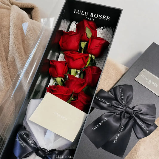 Nine red long-stem preserved roses presented in an open gift box with a greeting card.