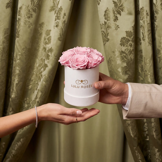 Person holding a small white box with pink roses against a green curtain background