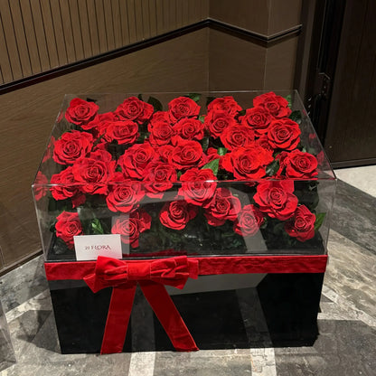 LULU ROSÉE Eternal Rose Garden 52 Red Roses in Clear Acrylic Box with Red Satin Ribbon on a marble floor