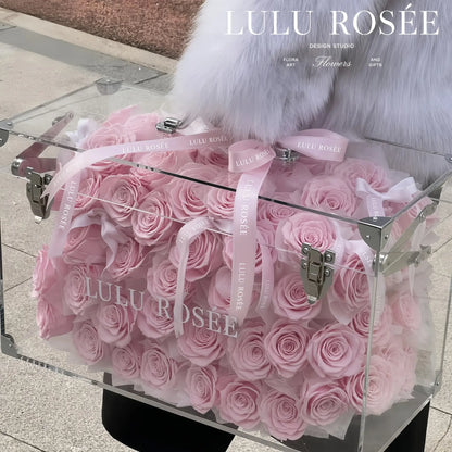 LULU ROSÉE Grande Eternal Acrylic Handbag Rose Box, luxury handbag-shaped transparent acrylic gift box filled with blush pink preserved roses, full front view with hand holding handle, customizable flower colors, romantic everlasting floral souvenir for anniversary & birthday gifting