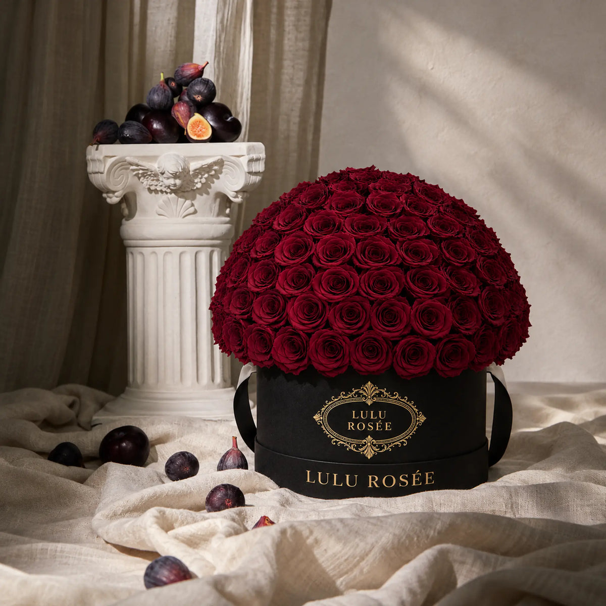 Burgundy preserved roses in a black LULU ROSÉE Large Le Plein box beside grapes.