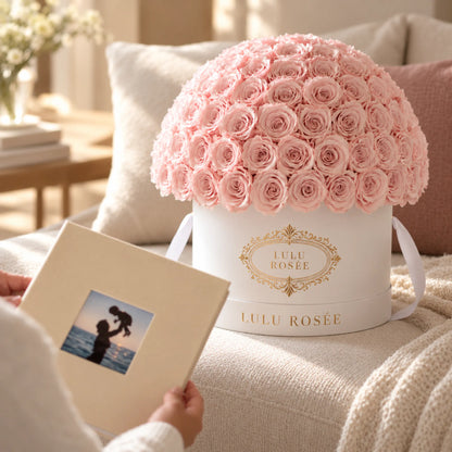 Light pink preserved roses in a white LULU ROSÉE Large Le Plein box beside a framed photo.