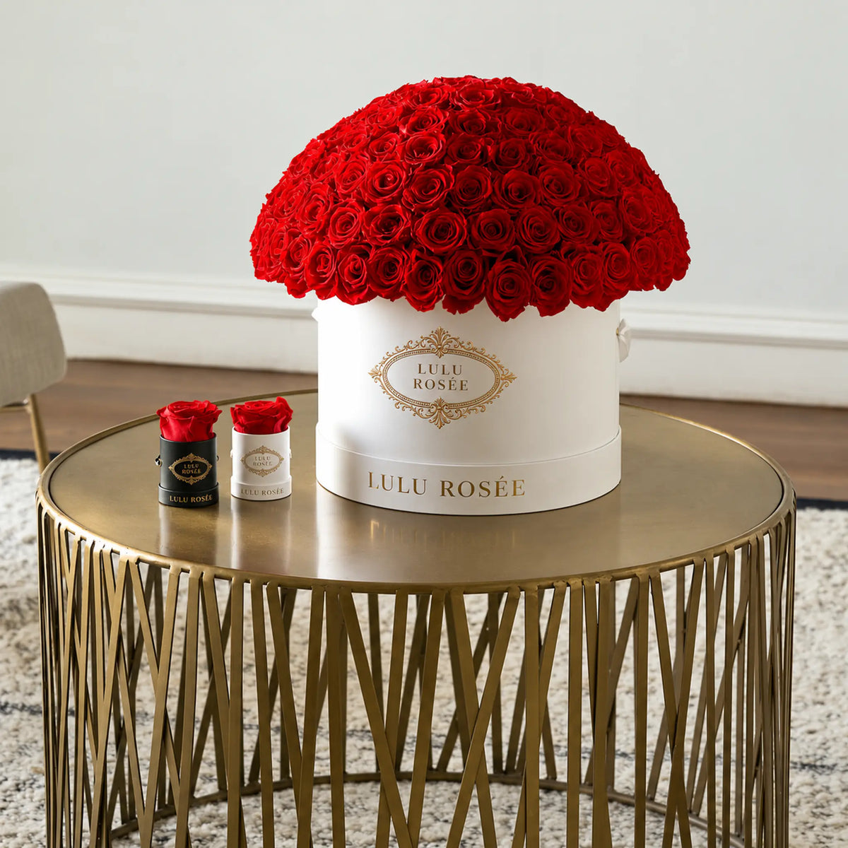 Red preserved roses in a white LULU ROSÉE Large Le Plein box on a gold side table.