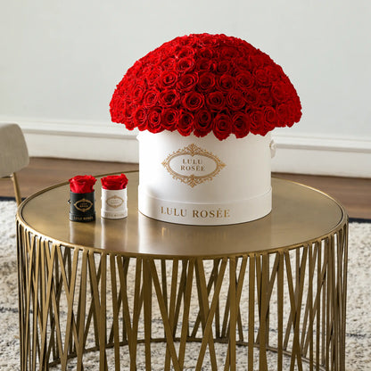 Red preserved roses in a white LULU ROSÉE Large Le Plein box on a gold side table.