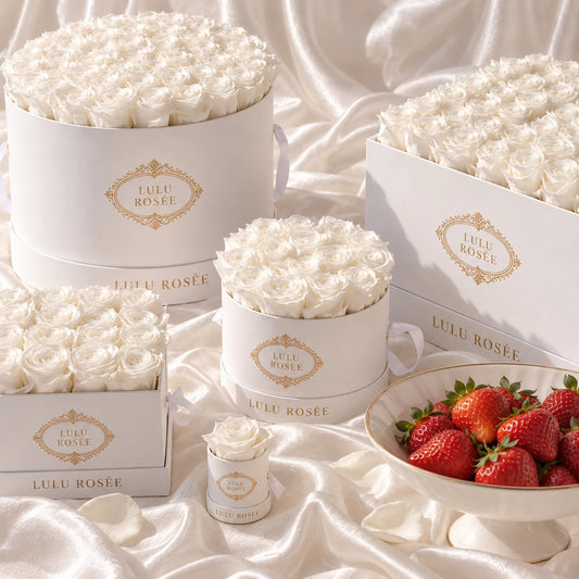 White preserved roses in round LULU ROSÉE boxes styled with strawberries on soft fabric.
