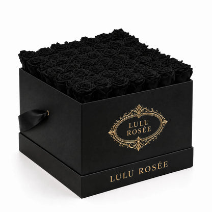 Black preserved roses arranged in a black classic LULU ROSÉE large square box on a white background.