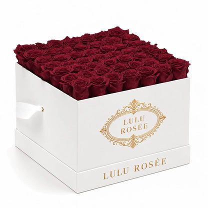 Burgundy preserved roses fill a white classic LULU ROSÉE large square box on a clean white background.