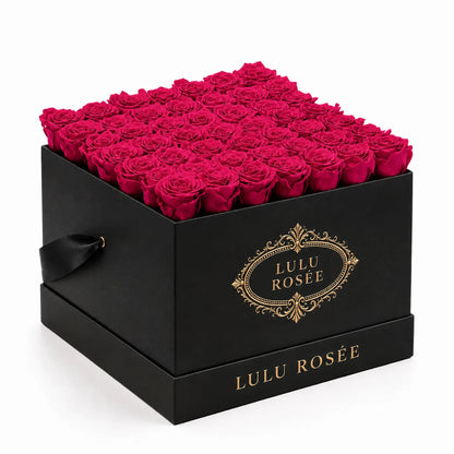 Hot pink preserved roses in a black classic LULU ROSÉE large square box on a white background.