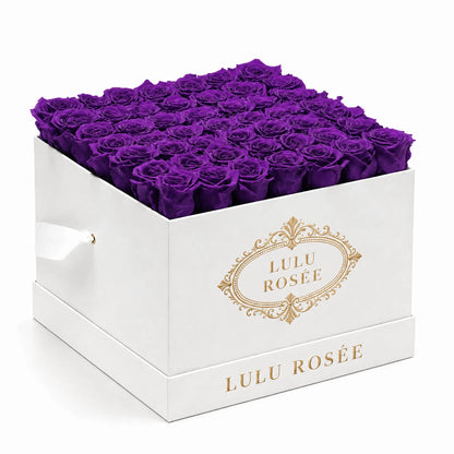 Purple preserved roses arranged in a white classic LULU ROSÉE large square box on a white background.