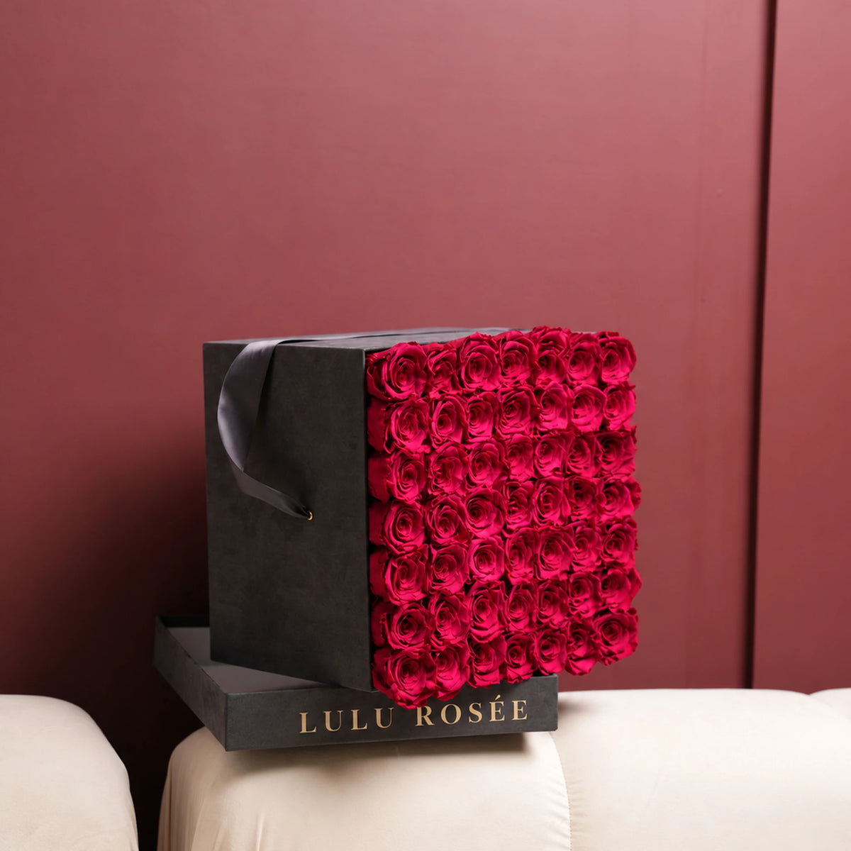 Red preserved roses in a Grey Suede LULU ROSÉE large square box, shown in a lifestyle setting.