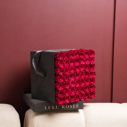 Red preserved roses in a Grey Suede LULU ROSÉE large square box, shown in a lifestyle setting.