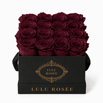 Burgundy preserved roses in a black classic LULU ROSÉE medium square box on a white background.