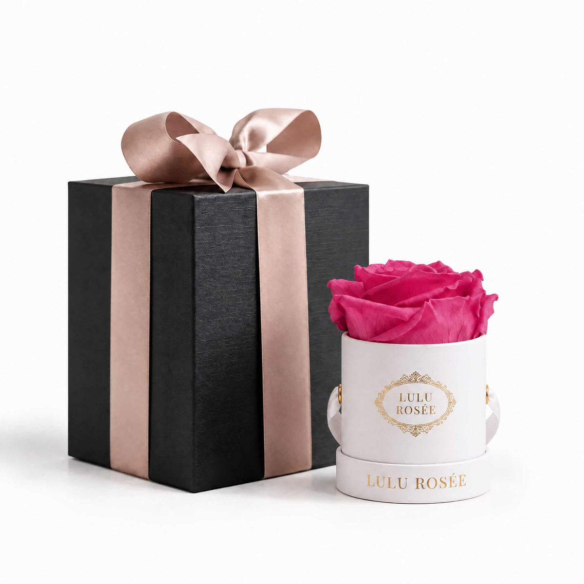 A light pink eternal rose in a white classic Mini Round box beside a wrapped gift box.
