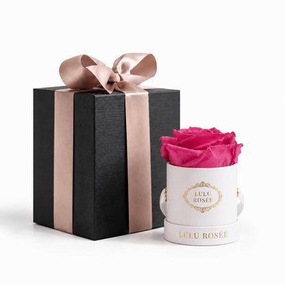 A light pink eternal rose in a white classic Mini Round box beside a wrapped gift box.