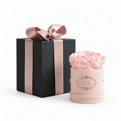 A pink eternal rose in a blush suede Mini Round box beside a wrapped gift box.