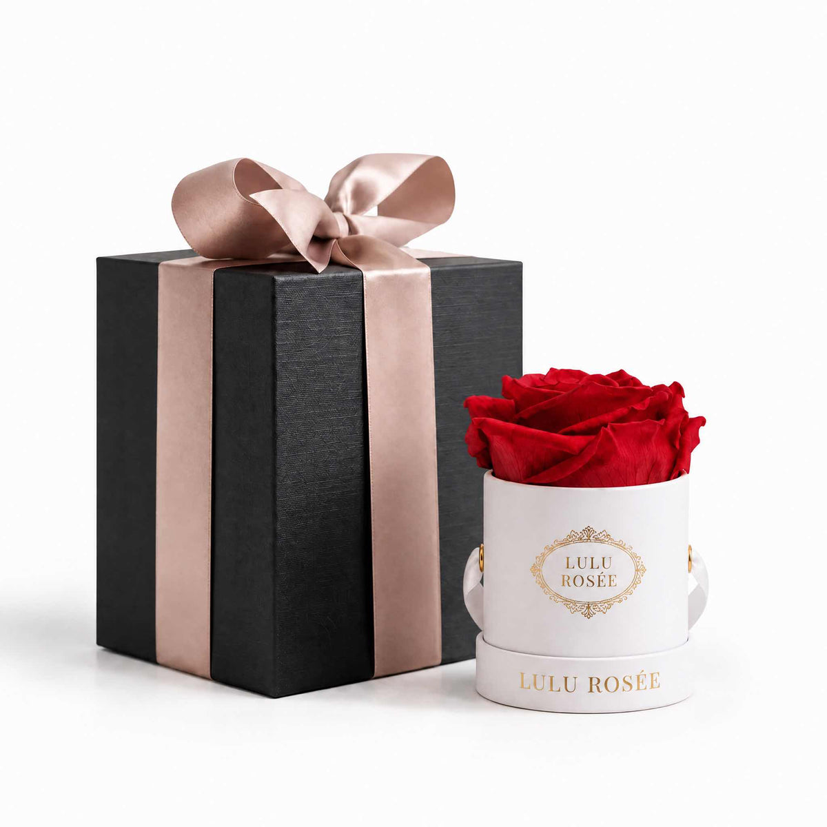 A red eternal rose in a white classic Mini Round box beside a wrapped gift box.
