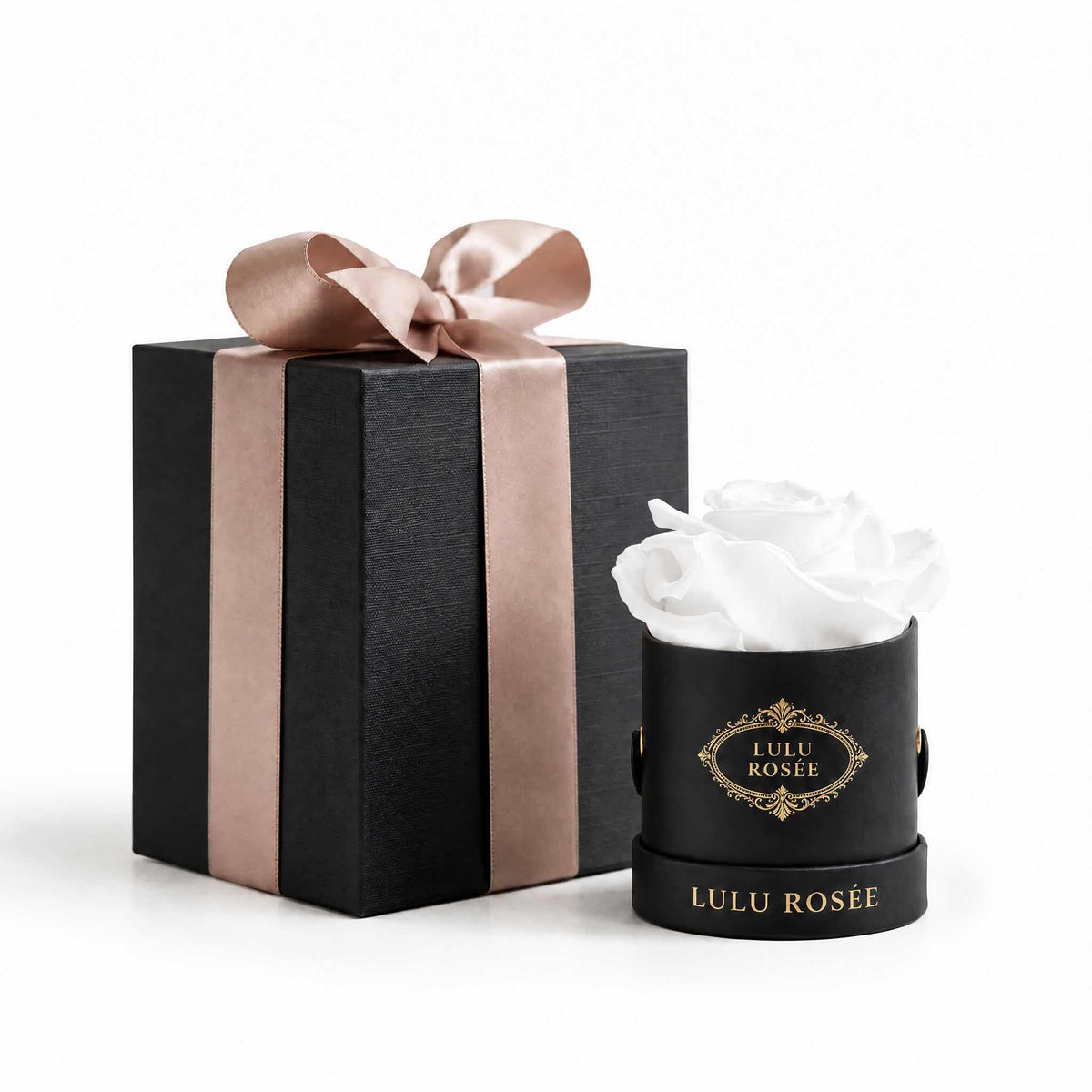 A white eternal rose in a black classic Mini Round box beside a wrapped gift box.