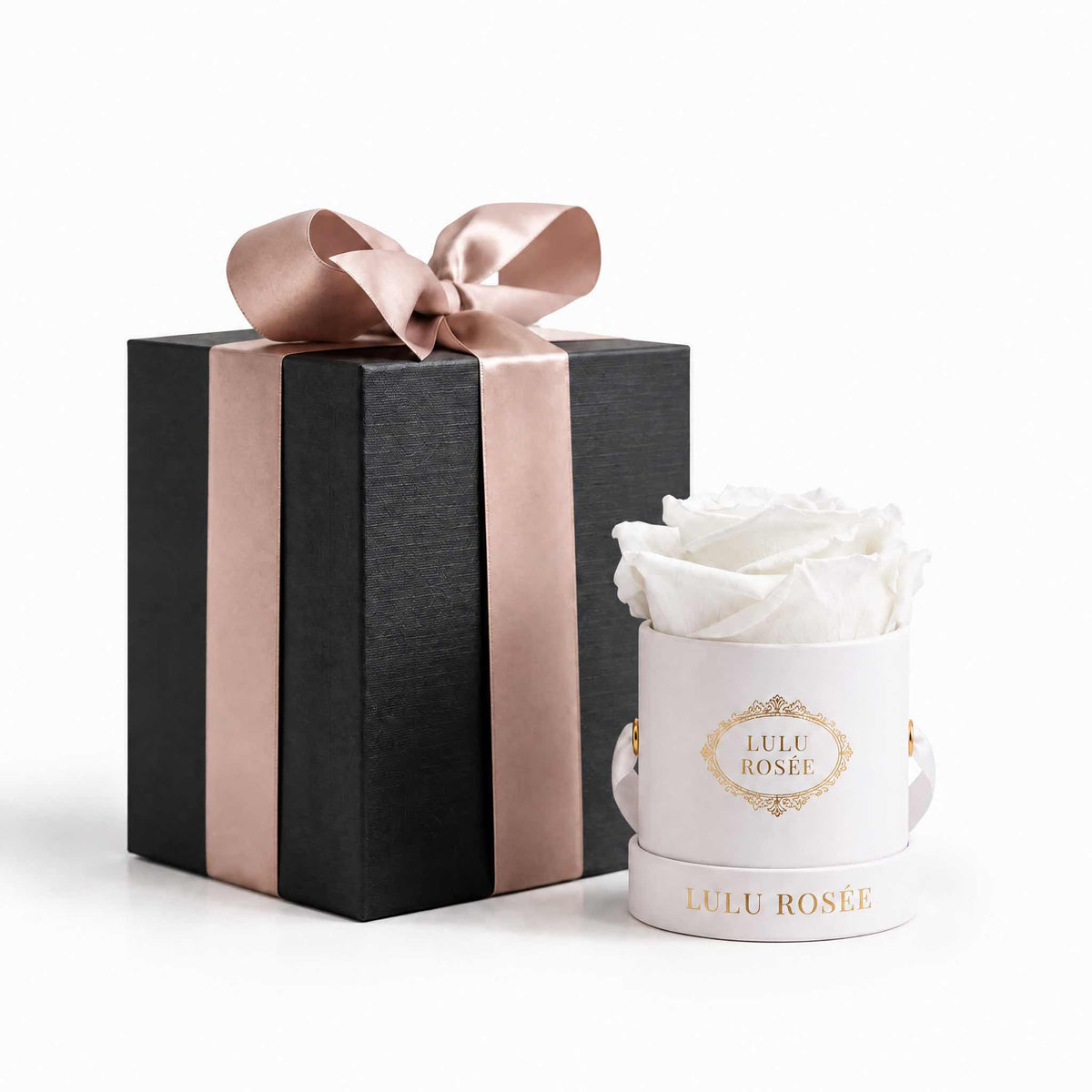A white eternal rose in a white classic Mini Round box beside a wrapped gift box.