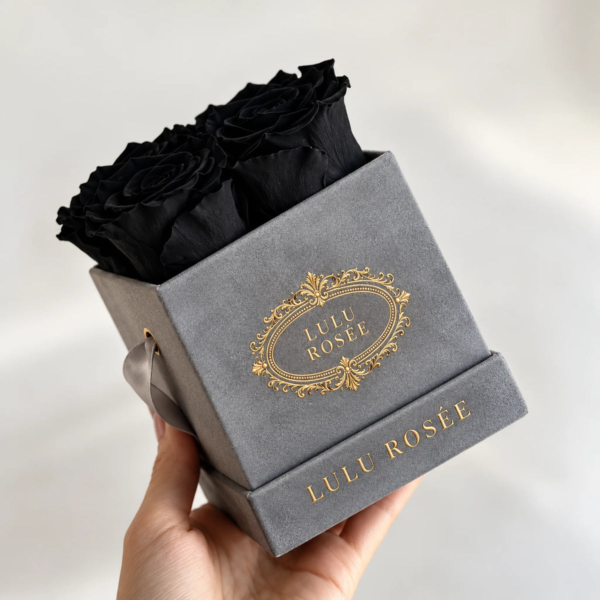 Grey suede box with black preserved roses, held in a hand