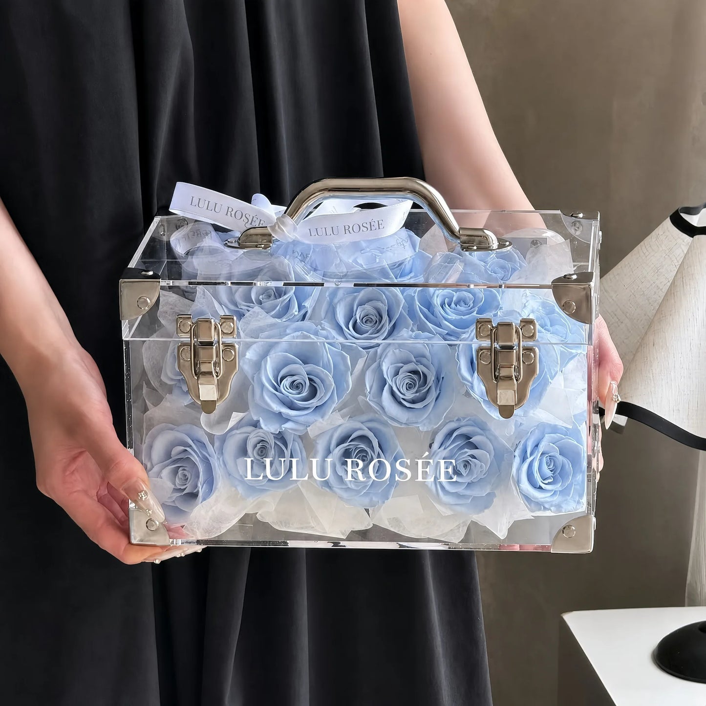 LULU ROSÉE Petite Eternal Acrylic Handbag Rose Box, small transparent acrylic handbag-shaped gift box filled with baby blue preserved roses decorated with pink satin bow, full front display shot, customizable flower color options, mini luxury everlasting floral souvenir for birthday, anniversary & romantic gift giving