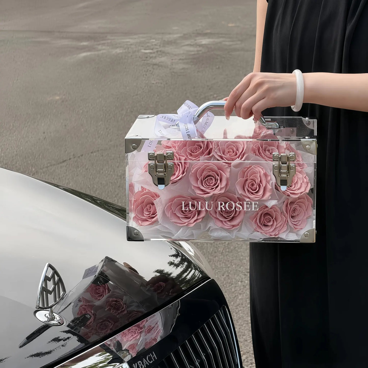LULU ROSÉE Petite Eternal Acrylic Handbag Rose Box, small transparent acrylic handbag-shaped gift box filled with blush pink preserved roses car interior closeup lifestyle shot, customizable flower color options, mini luxury everlasting floral souvenir for birthday, anniversary & romantic gift giving