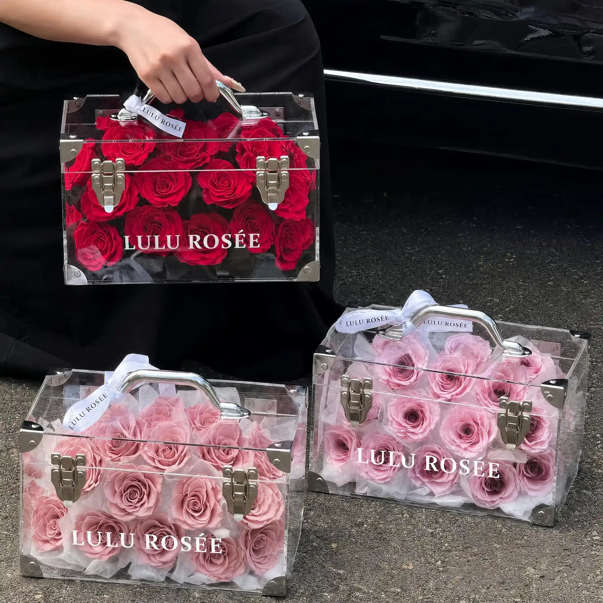 LULU ROSÉE Petite Eternal Acrylic Handbag Rose Box, small transparent acrylic handbag-shaped gift box, wine red & blush pink two box matching set shot beside car, customizable flower color options, mini luxury everlasting floral souvenir for birthday, anniversary & romantic gift giving