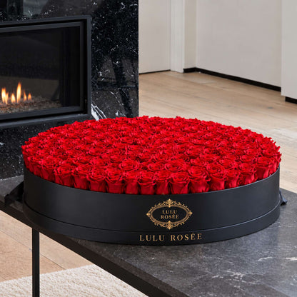 Red eternal roses in a Black Classic Round Grandiose box beside a fireplace
