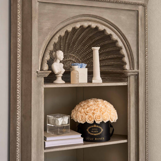 Light yellow preserved roses in a black classic Small Le Plein box displayed on an ornate shelf.