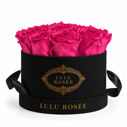 Hot pink preserved roses in a black small round box on a white background.