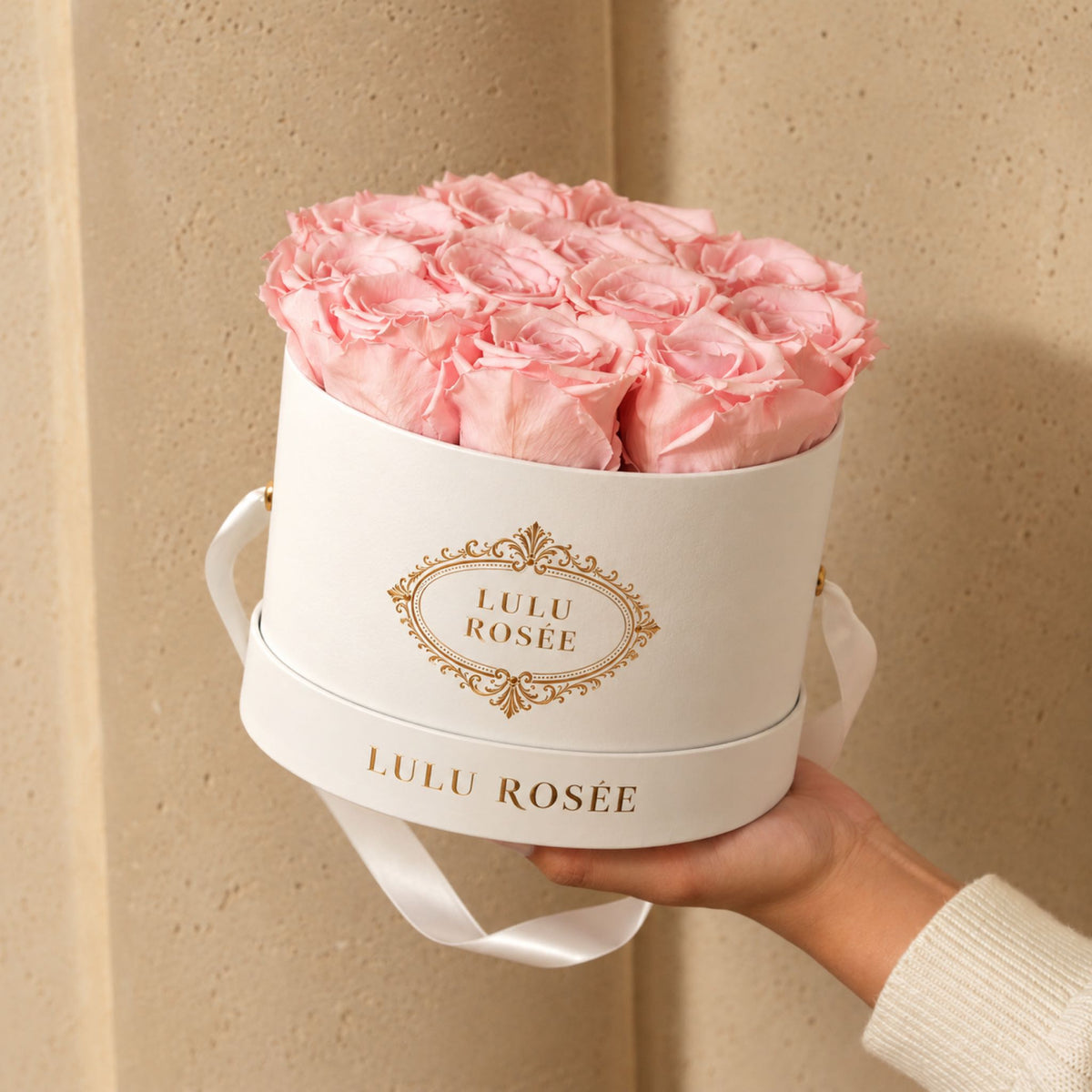 Light pink preserved roses in a white round gift box held by hand.