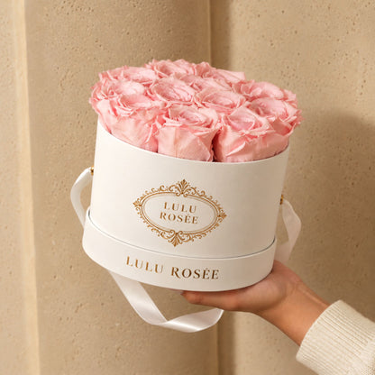 Light pink preserved roses in a white round gift box held by hand.