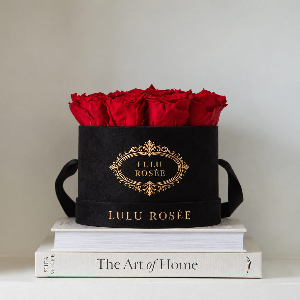 Red preserved roses in a black LULU ROSÉE round box styled on books in a home setting.