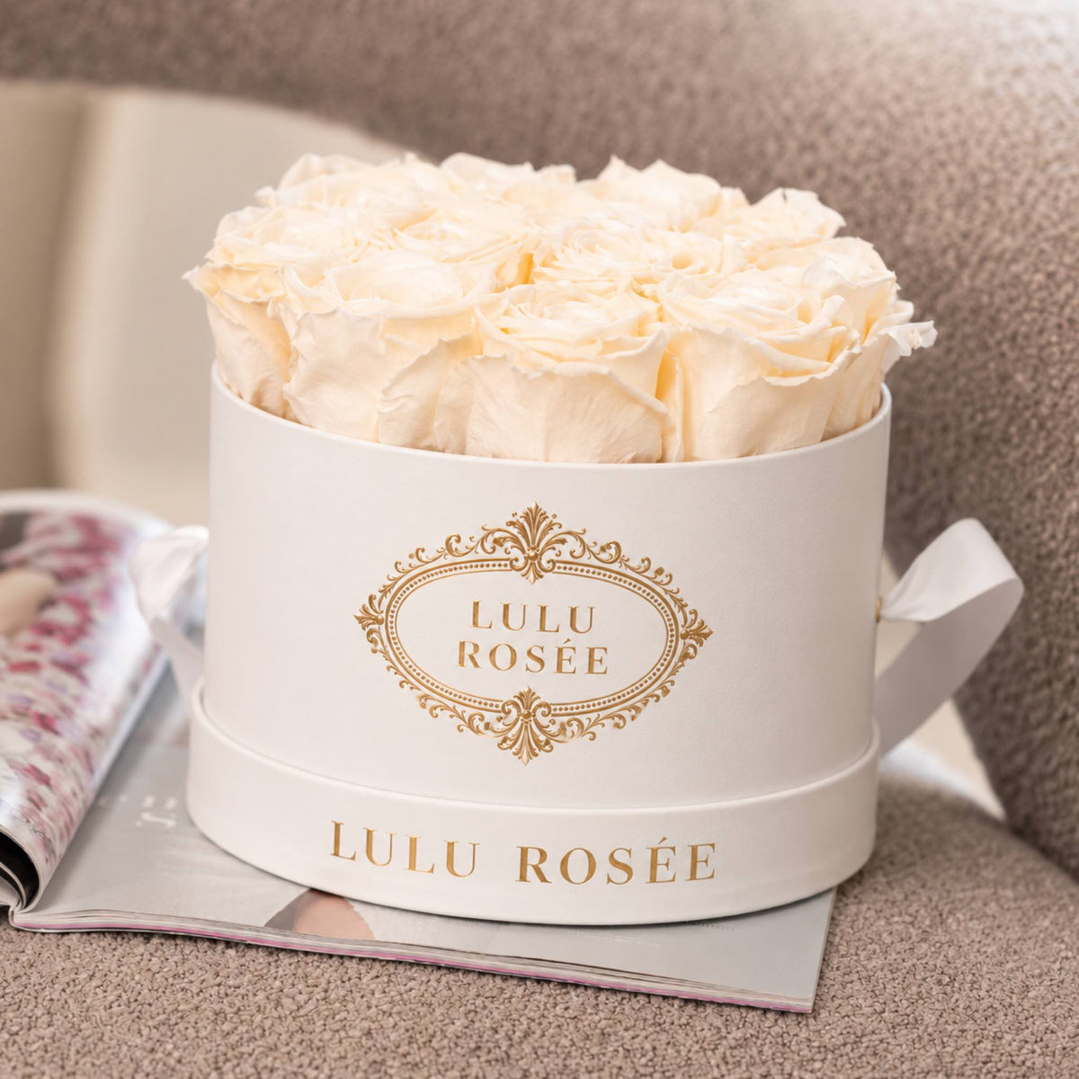 White preserved roses in a white classic round box, styled with magazines.