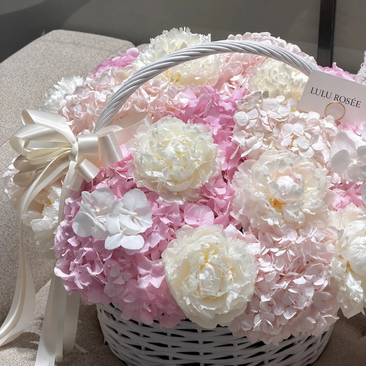 Cream bow beside white preserved peonies and blush hydrangeas in a flower basket