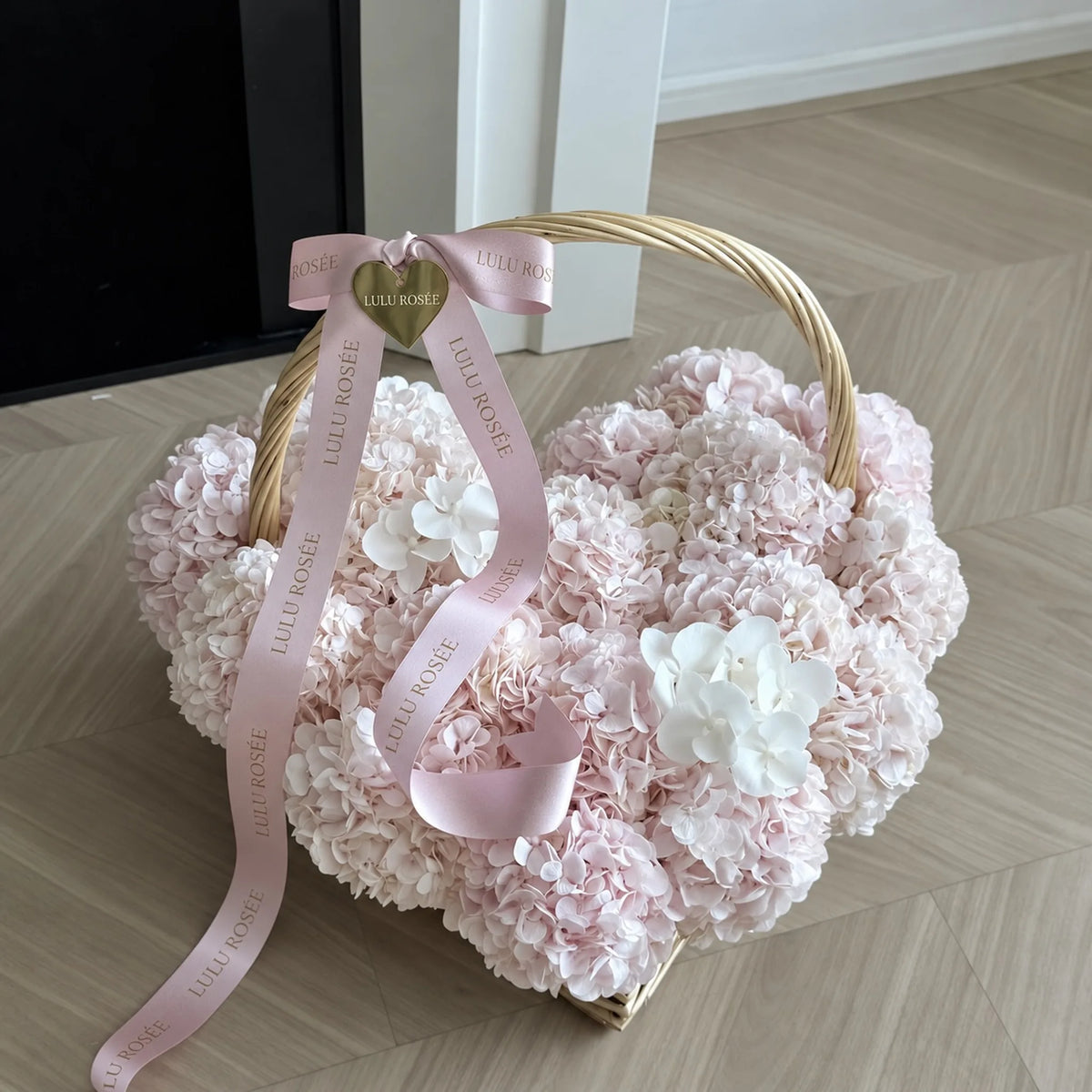 Angled view of a blush heart-shaped flower basket with a curved handle