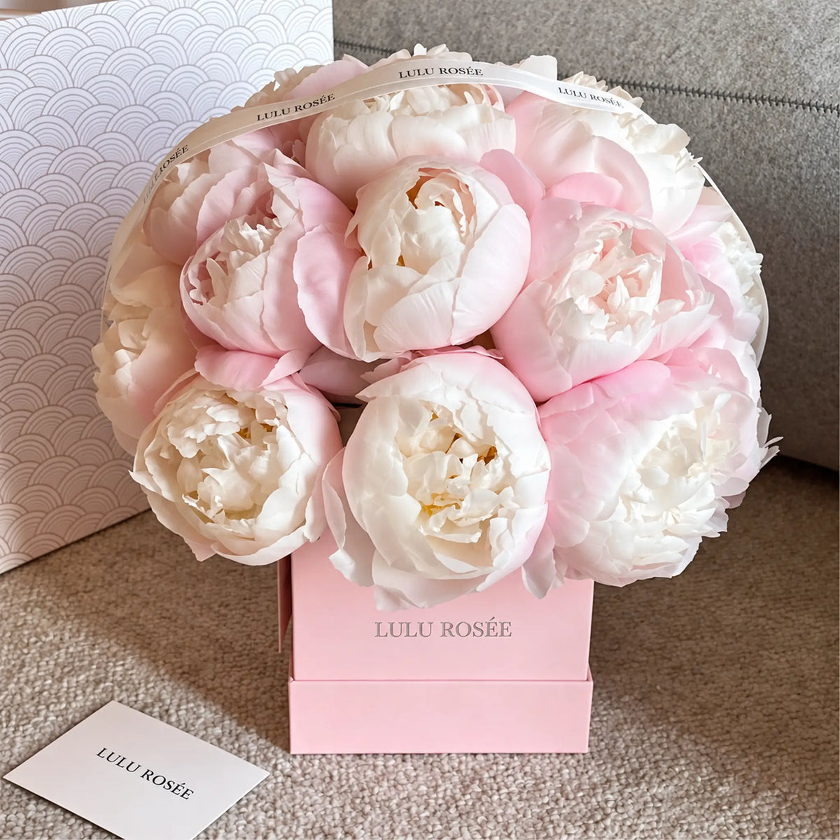 Blush preserved peonies in a pink LULU ROSÉE square box beside a card