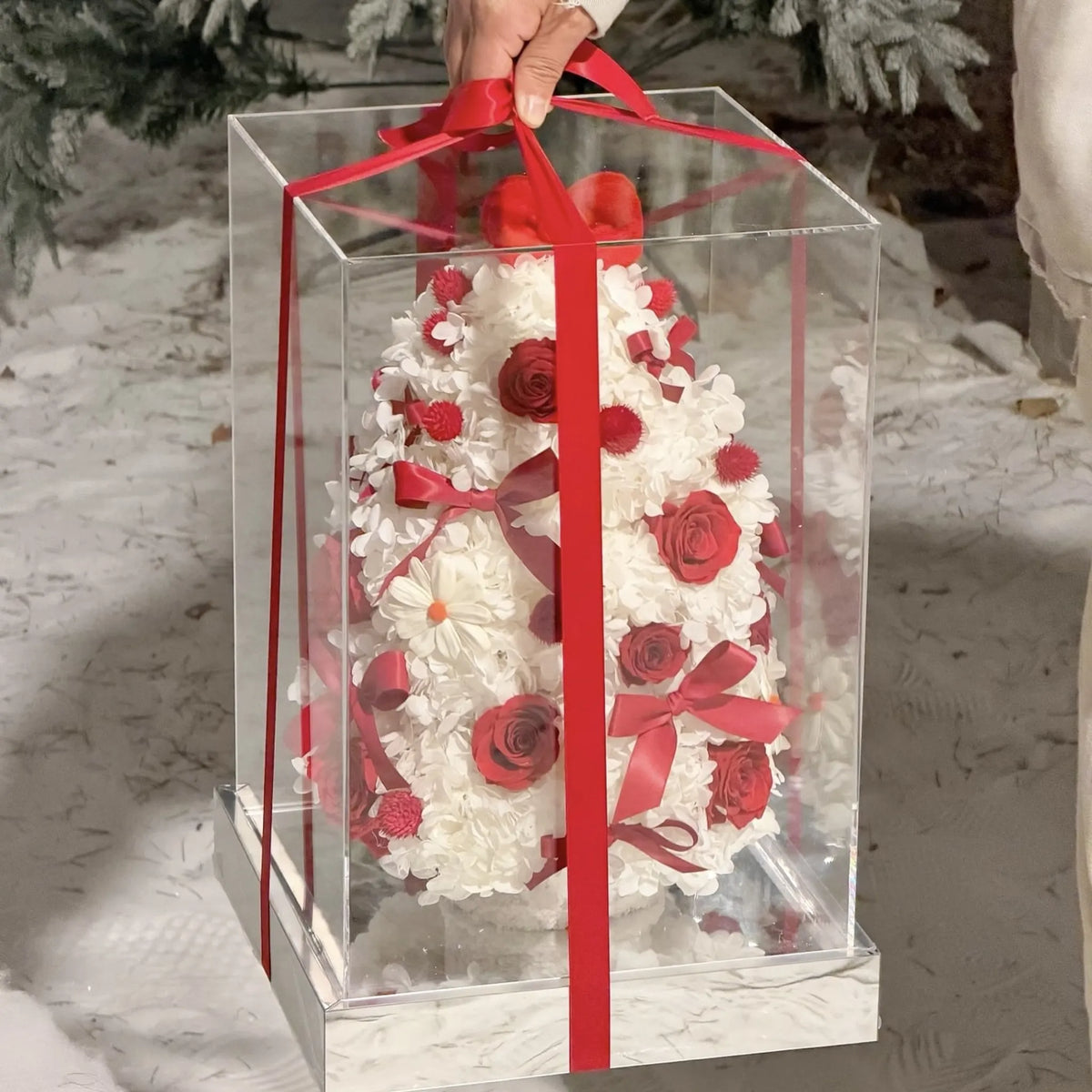Preserved flower Christmas tree in a clear presentation box tied with a red ribbon.