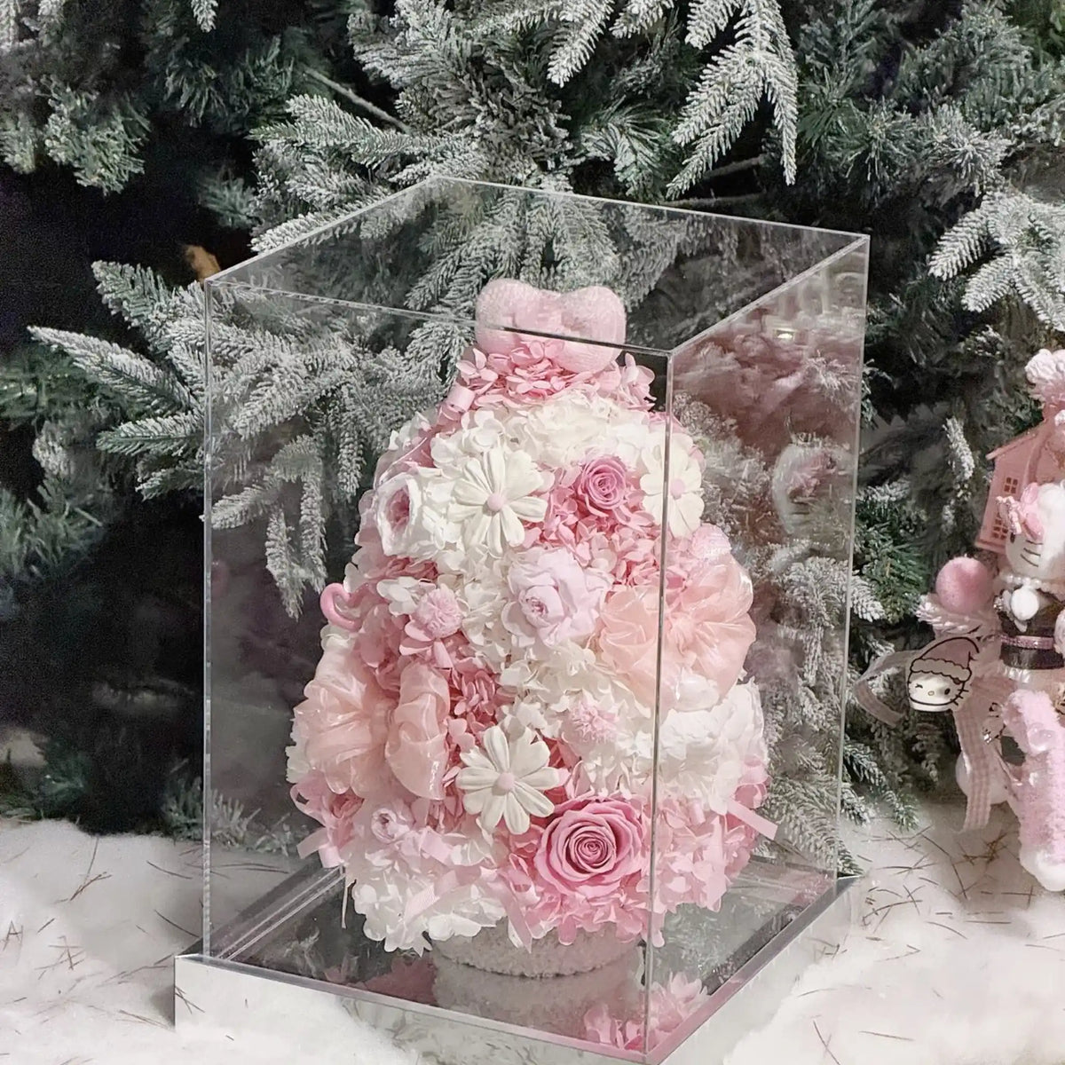 Pink preserved hydrangea Christmas tree inside a clear display box beside winter greenery.