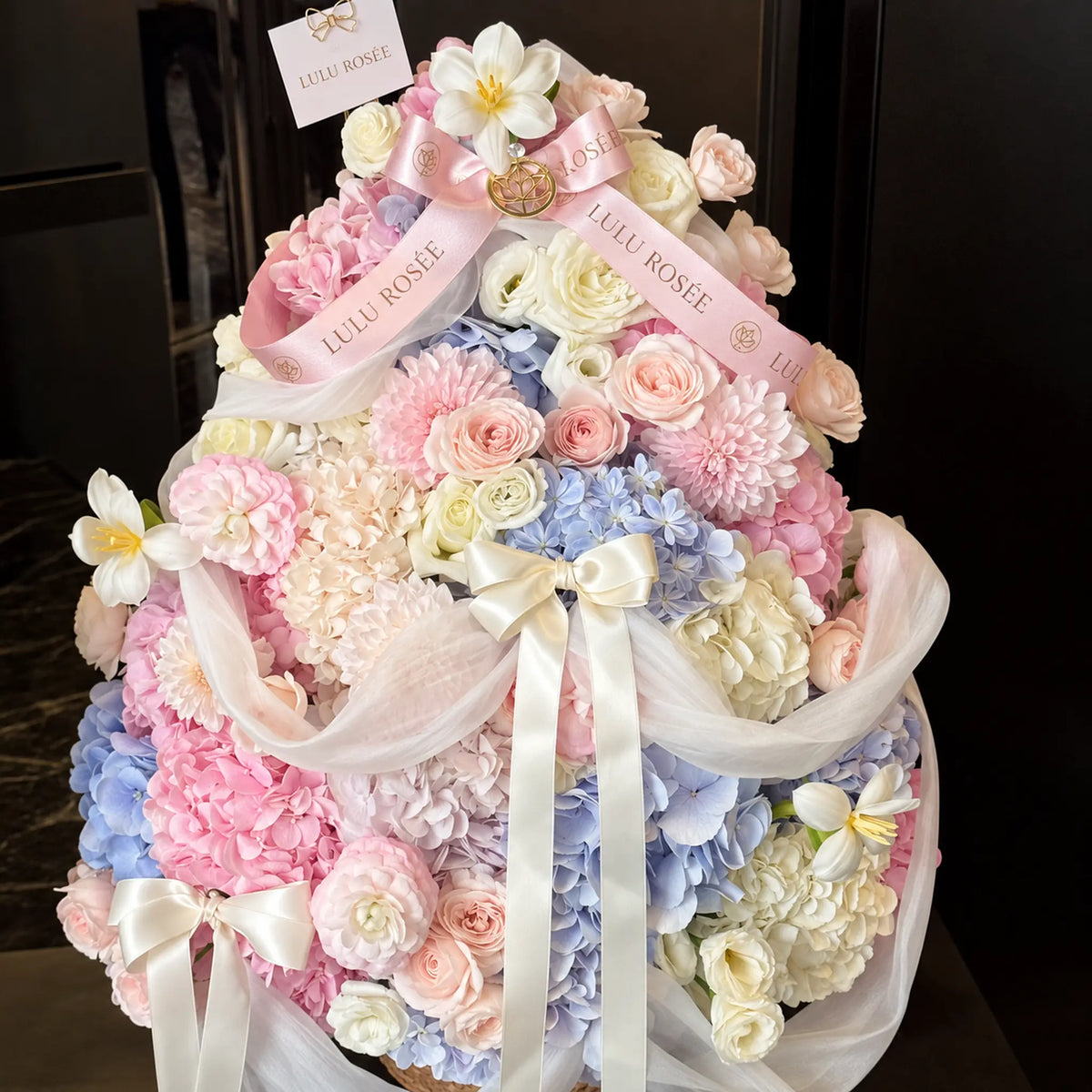 Front view of a Christmas inspired preserved flower arrangement with cascading white ribbons