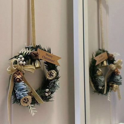 Small Christmas wreath with bell and cream bow hanging beside a mirror.