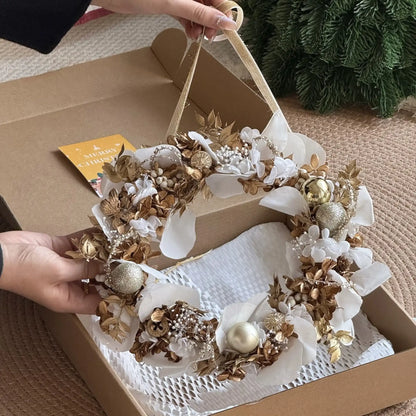 A person holds a white and gold preserved orchid and hydrangea wreath above its open gift box.