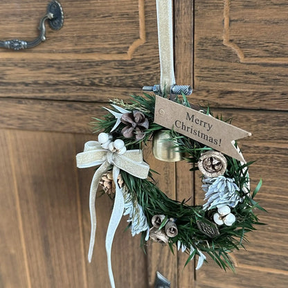 Small festive wreath with a bell, pale ribbon, pinecones and a Merry Christmas tag.