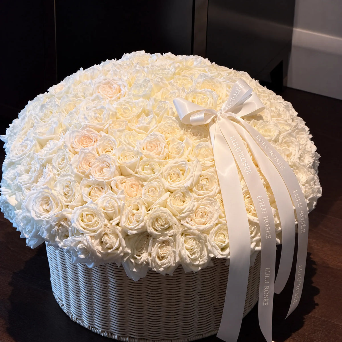 Cream preserved rose basket with long ribbons displayed against a dark interior